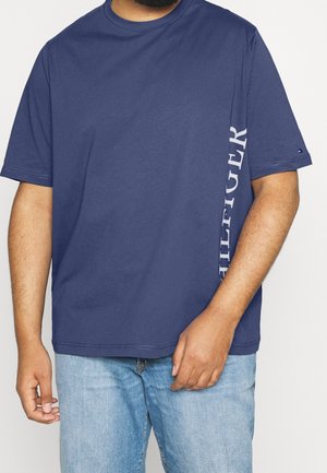 Mand iført en mørkeblå kortærmet T-shirt med "HILFIGER" trykt lodret på siden, paired med lyseblå denim jeans.