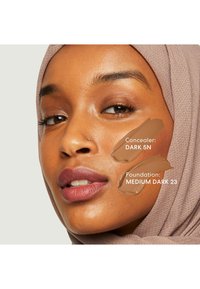 Il correttore nella tonalità Dark 5N e il fondotinta nella tonalità Medium Dark 23 sono stati applicati sulla guancia di una modella con un hijab marrone chiaro e una tonalità di pelle calda.