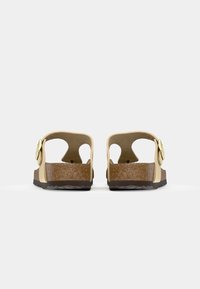 Die Schuhe verfügen über zwei Rückengurte und ein Blumendesign, bestehen aus leicht gelbem synthetischem Material, mit einer braunen Korksohle und strukturierter Oberfläche.