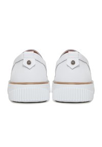 Paire de chaussures blanches décontractées sans lacets avec semelles épaisses et texturées, vues de dos sur fond blanc.