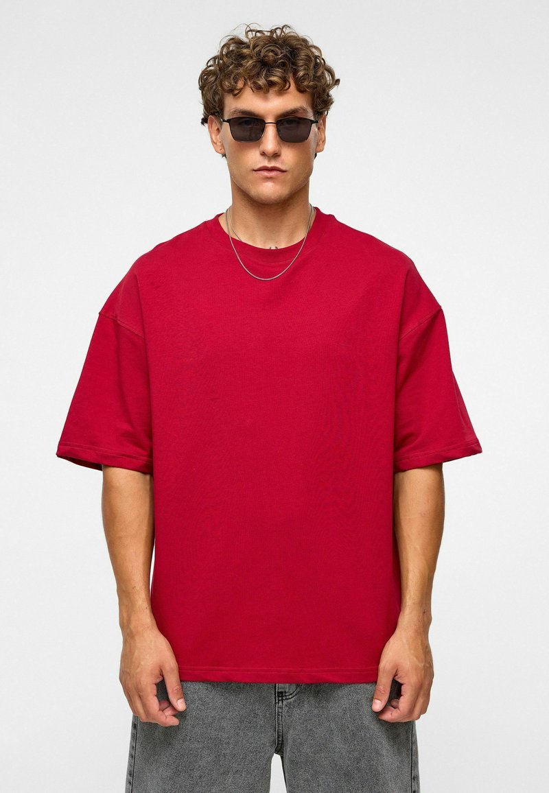 Rode katoen oversized t-shirt met korte mouwen, ronde hals en een relaxte pasvorm, gedragen met grijze denim broek en donkere zonnebril.