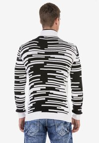 Gestreifter Strickpullover in Schwarz-Weiß mit gerippter Textur, hohem Kragen und kontrastierenden Linienmustern auf dem Rücken und den Ärmeln.