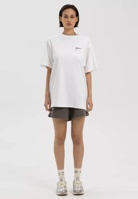 Witte T-shirt met korte mouwen en een soepele pasvorm, gecombineerd met grijze shorts. Opvallend merkimprint op het shirt. Model draagt sneakers en sokken.