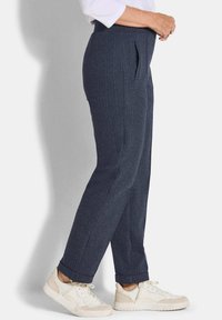 Donkerblauwe herringbone broeken met een hoge taille, zijzakken en opgerolde cuffs, gecombineerd met lichte sneakers. Geweven stofafwerking.