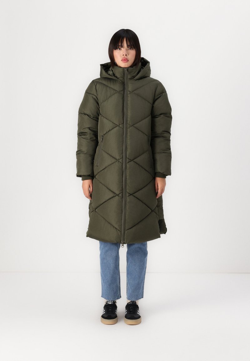Manteau matelassé vert olive avec capuche, présentant un motif de quilting diagonal, fermeture éclair et poches latérales, porté sur un jean bleu clair.