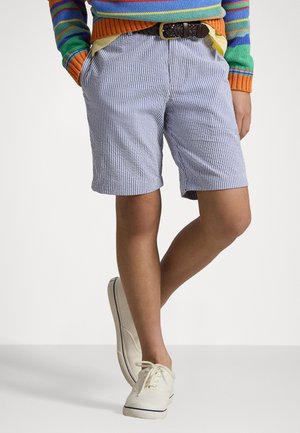 Pantaloni corti in cotone a righe blu e bianche con una vestibilità comoda, abbinati a scarpe in tela di colore chiaro e dotati di una cintura intrecciata marrone.