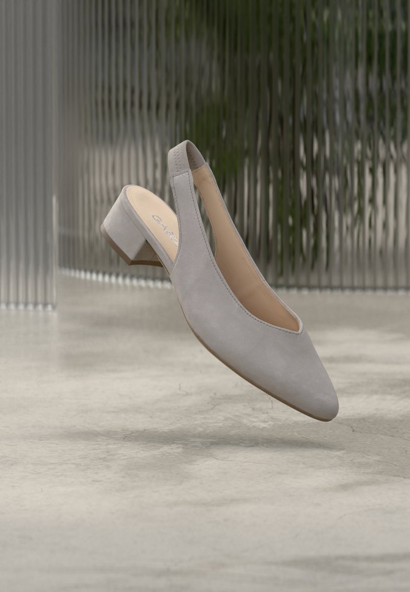 Chaussure slingback en daim gris avec un bout pointu, un petit talon carré et des découpes latérales. Texture lisse et design minimaliste.