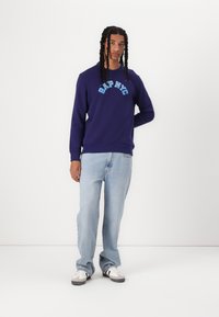Purple sweatshirt with "GAP NYC" graphic in light blue, paired with light blue jeans and black-and-white sneakers.