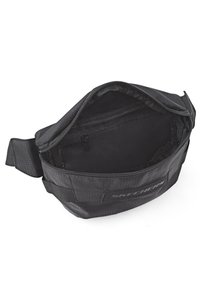 Bolsa de cintura de tela negra con apertura con cremallera, que muestra un interior principalmente vacío y una textura suave. Cuenta con una correa lateral y un detalle de logo.