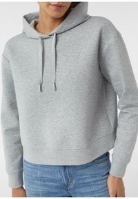 Osoba ubrana w jasnoszary krótki hoodie ze sznurkami oraz jasnoniebieskie dżinsy, pokazana od ramion do bioder na jednolitym tle.