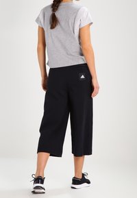 Szara bluzka z krótkim rękawem w połączeniu z czarnymi spodniami kulotami. Spodnie mają logo Adidas na tylnej kieszeni. Całość dopełniają czarne buty sportowe.