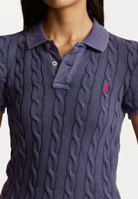 Fialová pletená polokošile s kabelovým vzorem, dvěma knoflíky na límci a malým růžovým logem na levé straně hrudi.