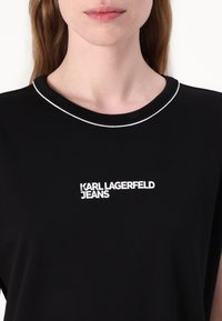 Čierne tričko s okrúhlym výstrihom a bielym akcentom. Na prednej strane sa nachádza biely nápis "KARL LAGERFELD JEANS".