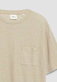 Chemise tricotée beige à manches courtes avec texture, col rond et petite poche poitrine.