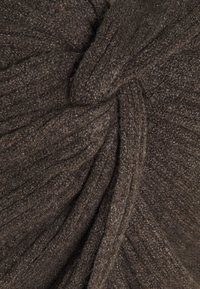 Brązowy materiał o teksturowanej powierzchni z prążkowanym wzorem, z twisted (kręconymi) sekcjami tworzącymi wymiarowy detal. Miękki, przytulny materiał o ciepłej tonacji.