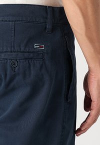 Tmavě modré chino kalhoty z bavlněné směsi, s texturovaným povrchem, zadní kapsou na knoflík a malou nášivkou s logem značky.