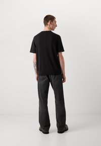 Zwarte shirt met korte mouwen en een ronde halslijn, een gladde textuur en een subtiele naaddetails die in het midden lopen, gecombineerd met donkerdenim jeans.