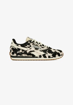 Teniska Reebok s černo-bílým vzorem krav, bílými tkaničkami, gumovou podrážkou a logem Reebok na boku, jazyku a patním límci.