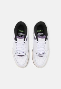 Zapatillas blancas con detalles en morado y verde, puntera perforada, cordones planos y suela de goma texturizada. Forro interior negro visible.