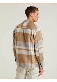 Camisa de cuadros en marrón, gris y blanco con mangas largas, puños abotonados y cuello. Confeccionada en una tela suave y texturizada.