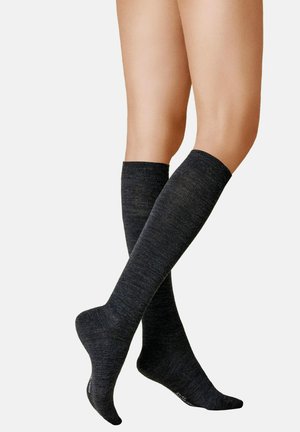 Beine, die dunkelgraue knielange Socken mit glatter, leicht melierter Textur vor einem schlichten hellen Hintergrund tragen.