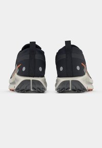 Schwarze Sportschuhe mit strukturiertem Obermaterial, einem Zuglaschen, reflektierenden Details und einer weißen Gummisohle mit gemustertem Profil.