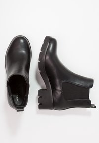 Czarne skórzane botki za kostkę z elastycznymi panelami bocznymi i grubą gumową podeszwą. Projekt charakteryzuje się okrągłym czubkiem i małą pętelką z tyłu.