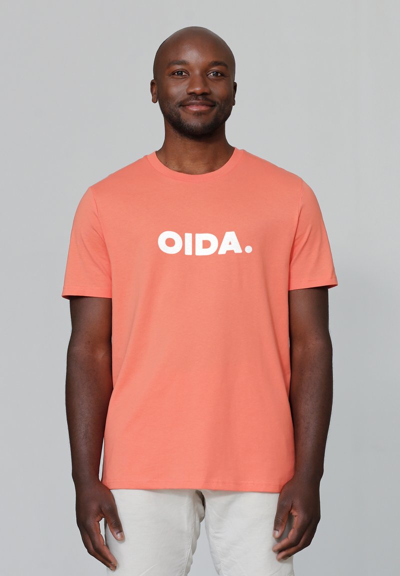 Korallefarbenes T-Shirt mit kurzen Ärmeln aus Baumwolle, auf der Vorderseite mit dem auffälligen weißen Text "OIDA.". Einfacher, runder Ausschnitt, lockere Passform.