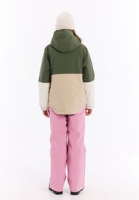 Veste bicolore avec des panneaux verts, beiges et blancs ; pantalon imperméable rose ; bonnet en tricot texturé. Vêtements décontractés pour l'extérieur.