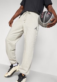 Svijetlosive trenirke s crnim Jumpman logom, elastična waistband i vezica. U paru s crnom i sivom košarkaškom loptom.