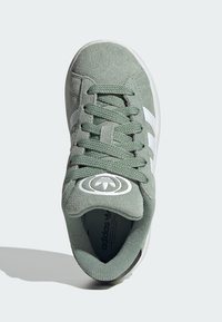 Zelené semišové tenisky s bielymi pruhmi, okrúhlym logom na jazyku, textúrovanými šnúrkami a gumovou podrážkou. Horný pohľad ukazuje tvar a dizajn.