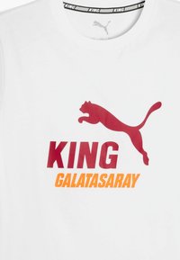 Camiseta blanca de algodón con un gran logo rojo de Puma y el texto "KING GALATASARAY" en negrita roja y naranja. Diseño clásico de cuello redondo.