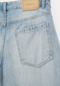 Lyseblå denimjeans med baglomme og tanfarvet læderbrandmærke "PULL&BEAR" syet over linningen.