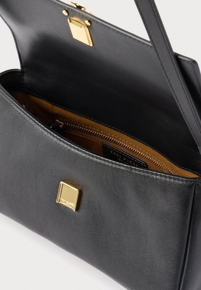 Black leather handbag with gold clasp and internal zippered pocket, open to show brown suede interior lining.