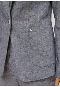 Blazer grigio in lino con tessuto testurizzato, presenta una chiusura con un singolo bottone e una tasca laterale visibile con un accento argento.
