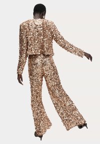 Skinnende rosaguld palietteret todelt sæt med en kort jakke og flagrende bukser, der har lange ærmer og en ensartet textur.