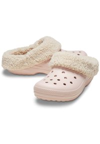 Zuecos de color rosa claro con un borde de pelo crema esponjoso. Presentan orificios de ventilación y una suela texturizada para mayor agarre. Diseño suave y acogedor.