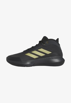 Chaussure de sport noire avec un design à trois bandes dorées sur le côté et une semelle rembourrée, vue de l'extérieur.