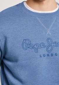Sudadera azul con un escote redondeado, que presenta bordado "Pepe Jeans LONDON" en hilo a juego. El material parece suave y texturizado.