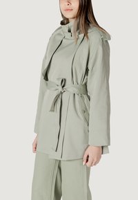 Giacca verde chiaro con cintura, colletto alto e dettagli con bottoni. Realizzata in un tessuto liscio, ha una vestibilità comoda e maniche lunghe.