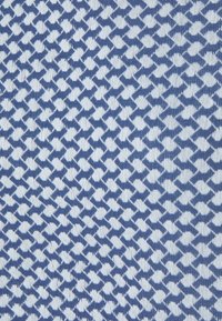 Blå och vit mönstrad tyg med en geometrisk design som har alternerande former, med en texturerad yta.