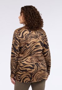 Camicia a maniche lunghe marrone e beige con motivo a strisce di tigre, tessuto liscio e polsini con bottoni, vista da dietro.