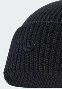 Zwarte gebreide beanie met een geribde textuur. Heeft een klein zwart logoaccent, een ronde vorm en flexibele stof voor comfort.
