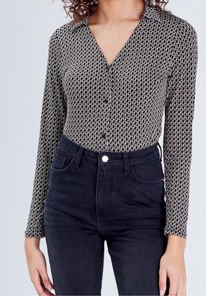 Femme portant une chemise noire et blanche à manches longues à motifs, rentrée dans un jean noir taille haute.