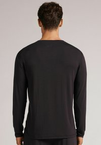 Černá košile s dlouhým rukávem vyrobená z měkké tkaniny, s kulatým výstřihem, volným střihem a jemnými švy na lemech.