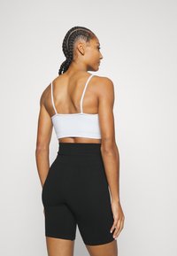 Sostén deportivo gris con tirantes finos y dobladillo acanalado. Pantalones cortos de ciclismo de tiro alto negros con una textura suave y un diseño ajustado. Estilo minimalista.
