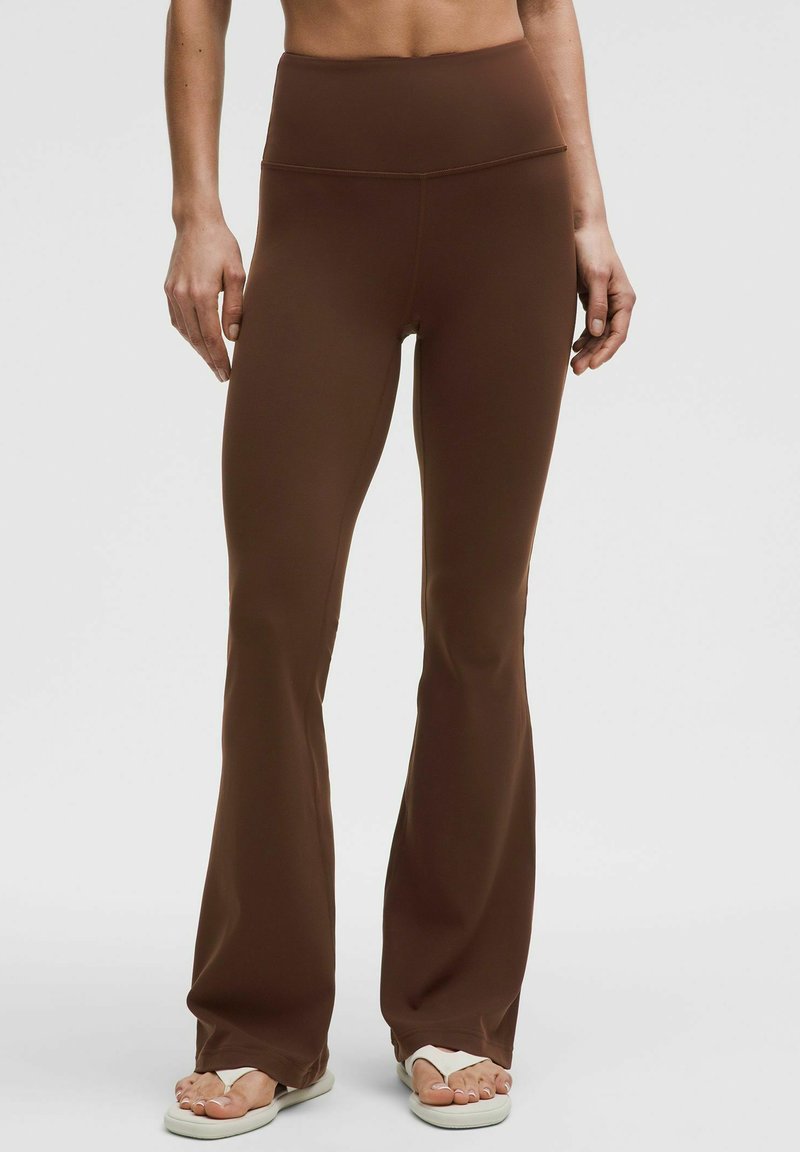 Braune schicke Leggings aus glattem, elastischem Stoff. Hoher Bund, leicht tailliert an den Oberschenkeln, mit weitem Saum. Einfaches Design.