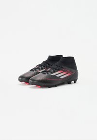 Black soccer cleats with a textured upper, featuring red accents and silver stripes. High ankle design with laces and molded studs.