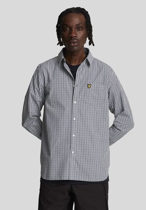 Zwart-wit geblokt shirt met lange mouwen, knoopsluiting en een klein geel logo op de borst. Klassiek ruitpatroon.