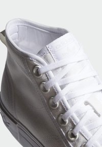 Zapatilla alta de lienzo blanco con cordones blancos, ojetes de metal y un interior acolchado. Presenta un logo en la lengüeta.